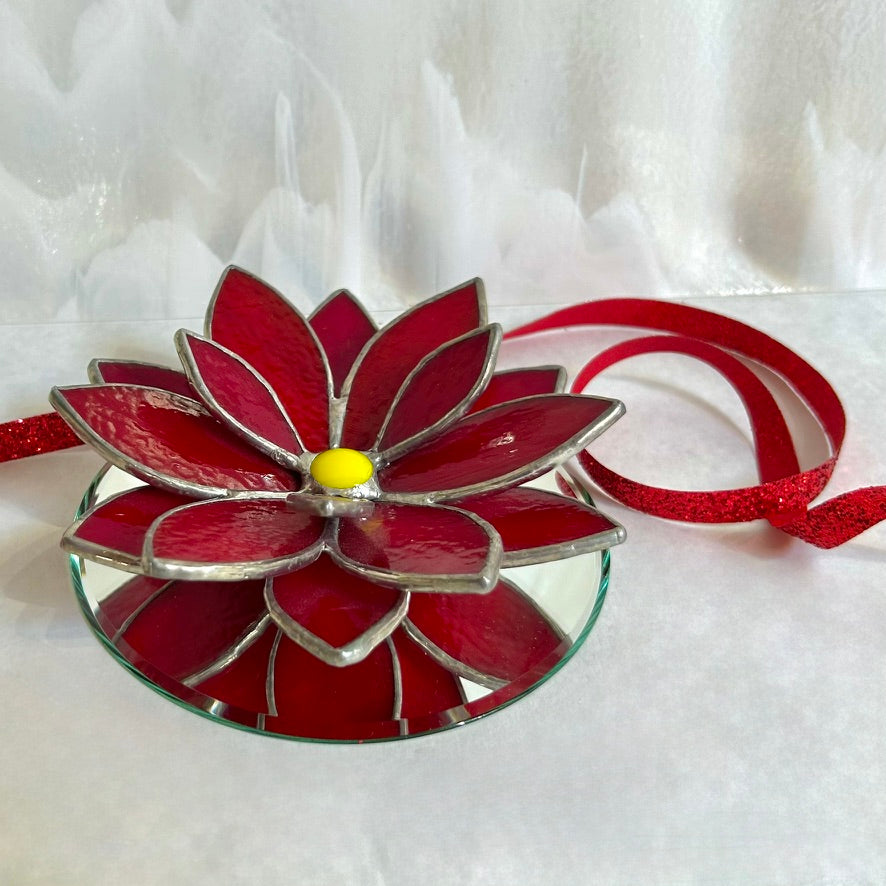 Stained glass poinsettia on a white backdrop with a red ribbon behind.